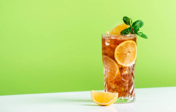 Long Island ice tea cocktail with vodka, rum, tequila, gin, liquor, lemon juice, cola and ice, garnished with lemon slice and mint in highball glass. Green background stock photo