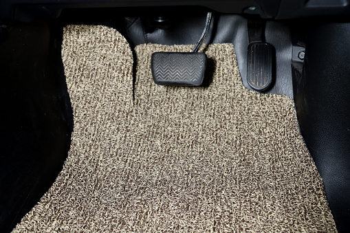 Clean the car floor mats from the beige carpet under the accelerator and brake pedals in the vehicle detailing workshop after dry cleaning.  Automotive service industry.  sedan interiors.