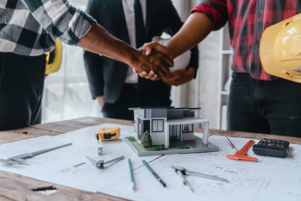 istock Shaking hands, Blueprints architects and building engineers talking meeting and planning will chronicle the design and technical aspects of a new house construction, renovation remodeling. 1457557010