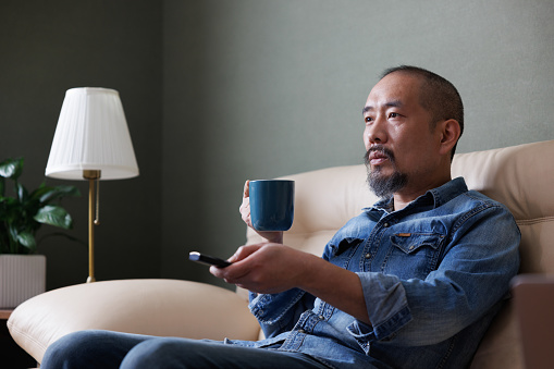 Asian middle-aged man sitting on the sofa watching TV