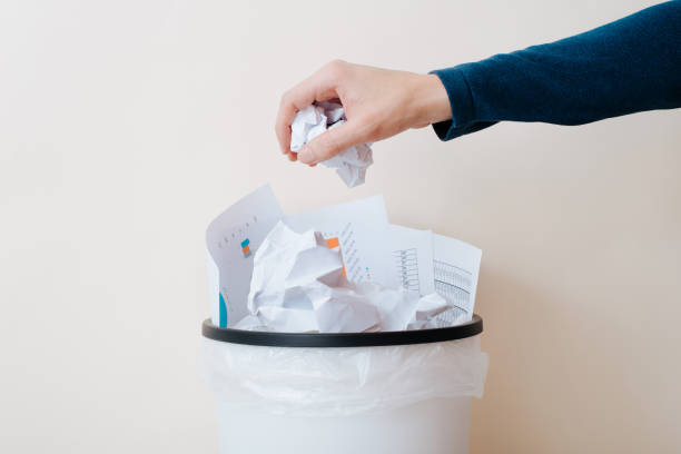 istock Close-up of an office worker's hand throwing crumpled paper documents into a trash can, indoors 1457568009
