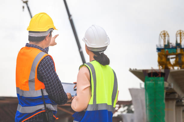 istock Female engineer and foreman worker checking project at building site, Engineer and builders in hardhats discussing on construction site, Teamwork concepts 1457575980