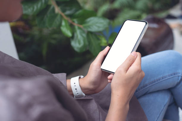 istock Mockup image of hand holding white mobile phone with blank black screen on thigh 1457579508