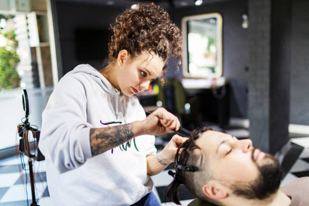 junge friseurin flechtet dem kunden im friseursalon haare - owner hair salon beauty spa female stock-fotos und bilder