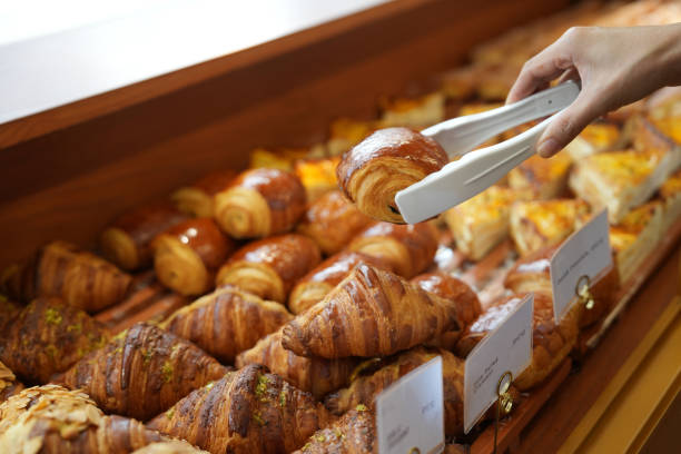 Close-up woman choosing pastry from a bakery store selecting holding a tray and service tong Cropped image of an Asian young woman buying pastry from a cafe selecting holding a tray and service tong bun bread stock pictures, royalty-free photos & images