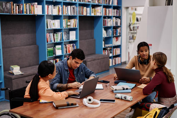 istock Diverse group of young people studying together sitting in library 1457587187