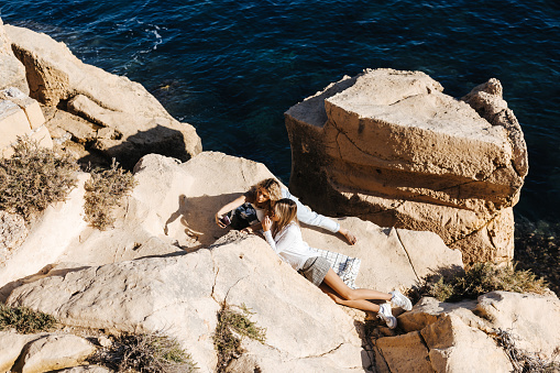 High angle view of young female friends taking selfie while lying on rock by the sea on sunny day