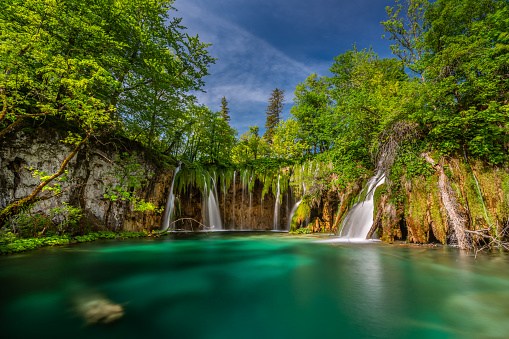 HDR image long exposure shot of beautiful lake with small waterfalls and lush green vegetation on sunny day in plitvice lakes national park in croatia
