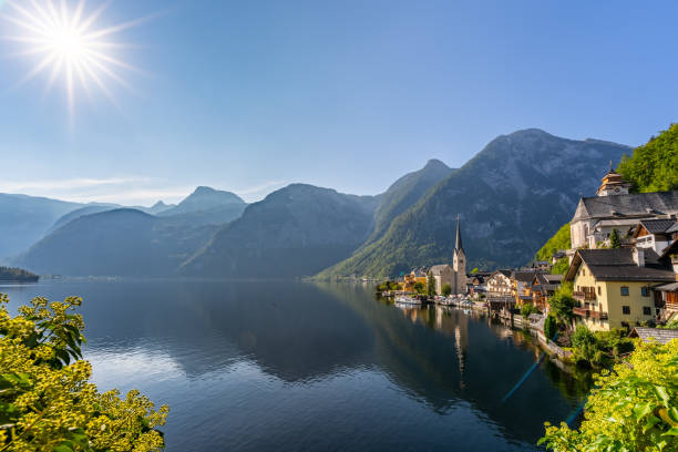 HDR image of calm lake Hallstatt on sunny day with star shape sun, reflections in the water and typical alpine houses of the village