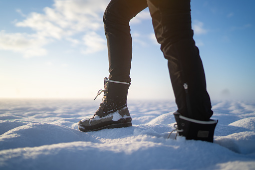 Woman in black trouser walking through fresh deep snow on wide field on cold winter morning, legs and boots, background blurred