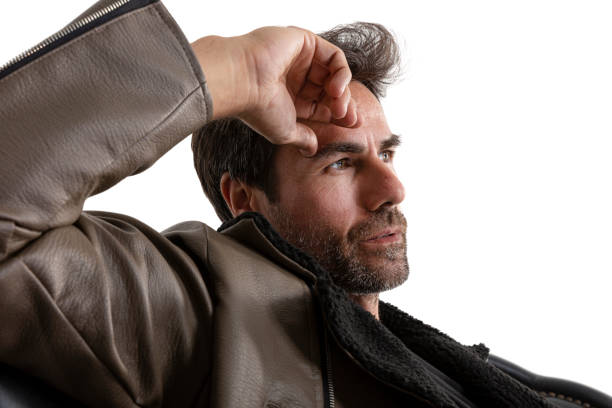 Handsome middle-aged hispanic stubby bearded man sitting on leather sofa. Short-haired handsome man in jacket, t-shirt and jeans, on white background. man wearing boots crosses legs.