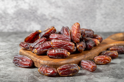 Date fruit on a dark background. Organic pile of medjoul dates on a wood serving board. Ramadan food. close up