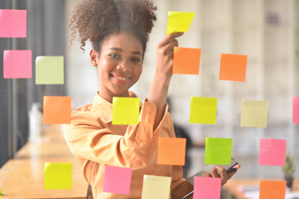 istock Confident African American woman putting sticker notes to share idea for startup project on glass board in modern office. 1457595838