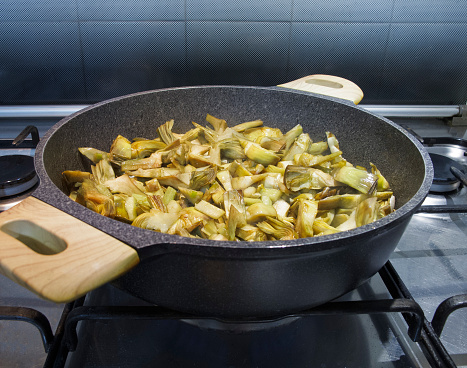 pan with cut artichokes, side view, while cooking on gas stove
