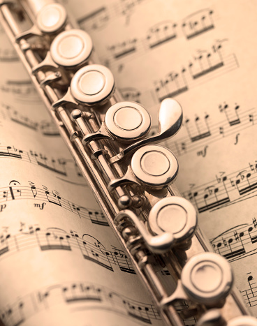 transverse flute resting on a classical music score, sepia-toned image
