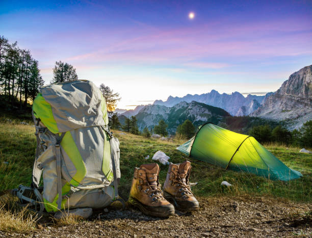 Hiking Equipment, Tent, Backpack and Boots under a moon night sky at amazing twilight hour. Alps, Triglav National Park, Slovenia. stock photo
