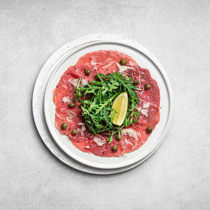 Beef carpaccio with capers, arugula and parmesan on a white plate