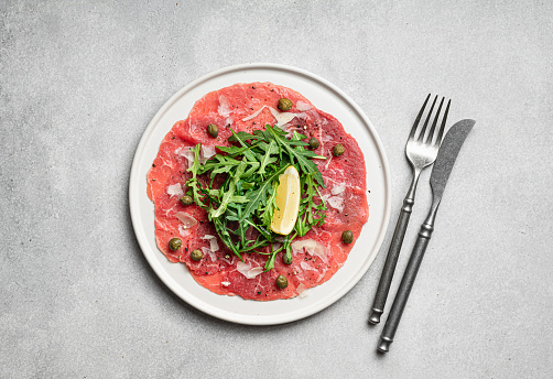 Beef carpaccio with capers, arugula and parmesan on a white plate