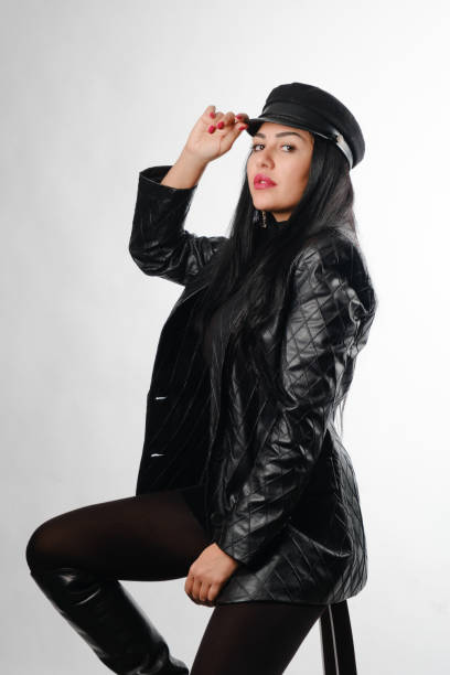 Beautiful brunette posing holding her hat in leather jacket sitting on bar stool