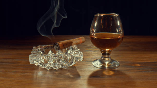 Ashtray with a light up cigar and a glass of alchohol drink stock photo