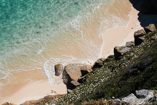Views down onto an empty idyllic beach with pristine sand and clear blue sea, South Cornwall near Porthcurno on a bright sunny June day.