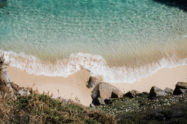 Views down onto an empty idyllic beach with pristine sand and clear blue sea, South Cornwall near Porthcurno on a bright sunny June day.