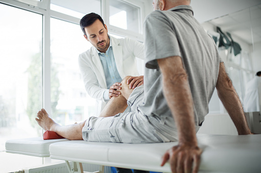 Closeup side view of a mature man having medical exam. The doctor is examining patient's knee for symptoms of arthritis and osteoporosis.