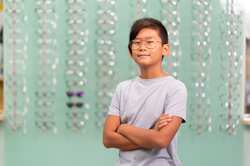 An asian boy trying on glasses in an optician store. Background with glasses showcase