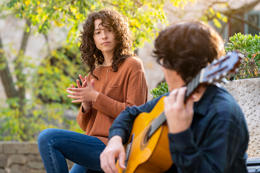 Brunette young curly woman singing with a guitarist man in the street