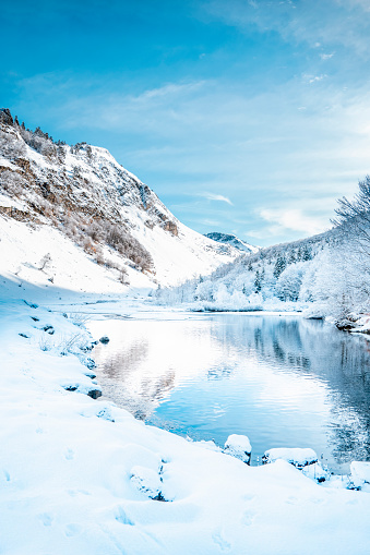 Picturesque landscape of a snowy winter mountain lake. Small lake next to the Saut Deth Pish waterfall during autumn and a snowy day, located in the Aran Valley, Pyrenees, Catalonia, Spain.