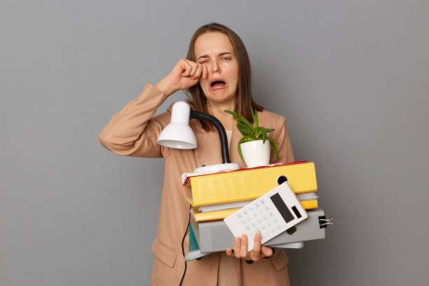 изображение отвергнутой отчаяния грустной женщины в стильной бежевой куртке, держащей офисные вещи, плачущей, потерявшей работу, уволенно� - life jacket despair business life стоковые фото и изображения