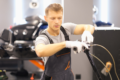 Man inspects motorcycle in repair shop. Motorcycle front fork repair concept