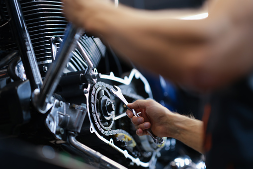 Male mechanic repairs amotorcycle motor with wrench in service center. Motorcycle maintenance and repair concept