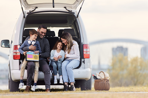 Happy parents and their kids talking while relaxing in a car trunk in nature. Copy space.