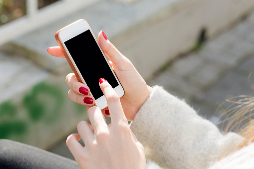 Close-up photo of female hands with smartphone. Young woman typing on a mobile phone on a street