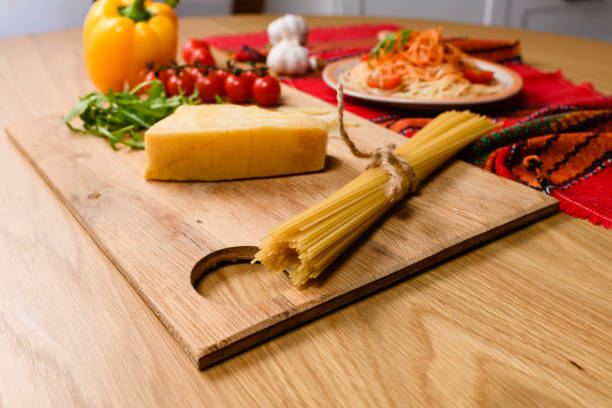 A bunch of whole grain spaghetti pasta tied with a string on a cutting board on a background of parmesan cheese, cherry tomatoes, cooked pasta.