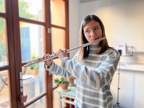 Young teenage girl playing the transverse flute at living room