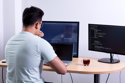 Programmer analyzing his recently completed programming work with three monitors in his office.