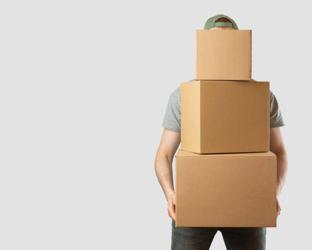 istock young man with cardboard box on a gray light background. Moving. Delivery. 1457643864