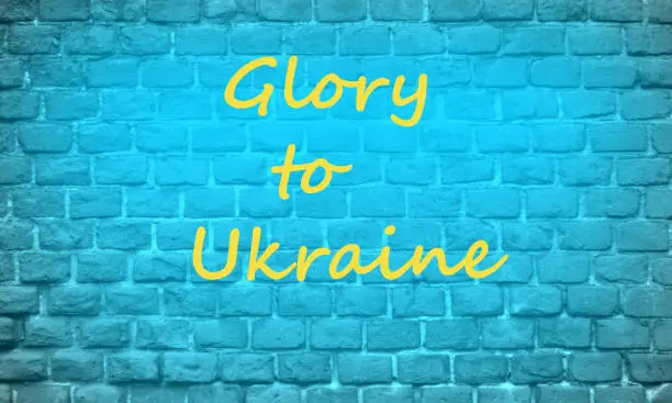 Brick blue wall with yellow inscription GLORY to Ukraine. Stop the war in Ukraine