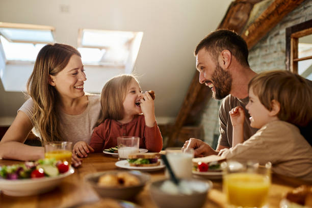 família jovem falando durante o café da manhã na mesa de jantar. - family togetherness eating meal - fotografias e filmes do acervo