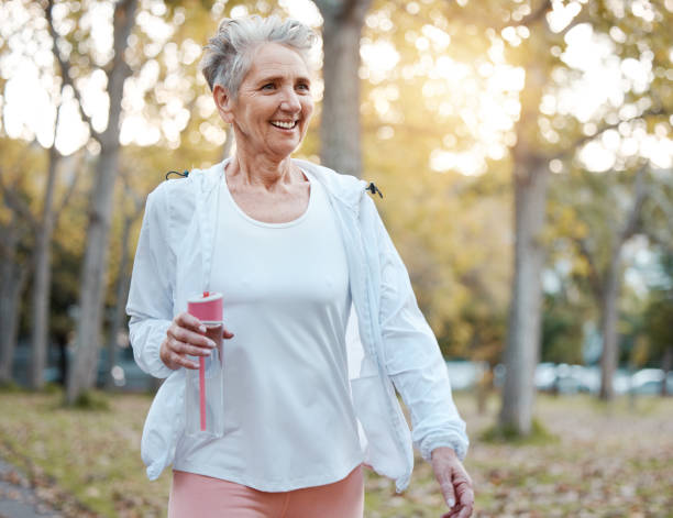 fitness, natura e donna anziana con borraccia per il benessere, l'idratazione e i minerali per passeggiare nel parco. salute, pensionamento e donne anziane che fanno allenamento, esercizio fisico e allenamento cardio all'aperto - real estate immagine foto e immagini stock