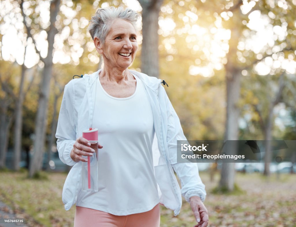 Fitness, nature and senior woman with water bottle for wellness, hydration and minerals for walking in park. Health, retirement and elderly female doing workout, exercise and cardio training outdoors Racewalking Stock Photo