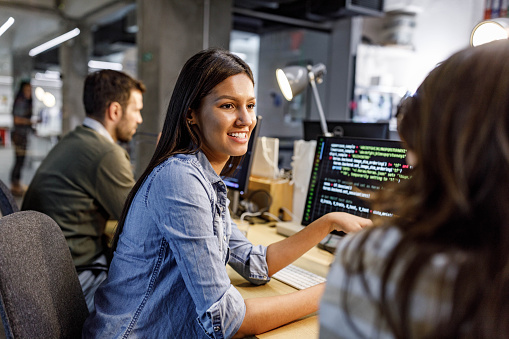 Happy female computer programmer communicating with her colleague while working in the office.