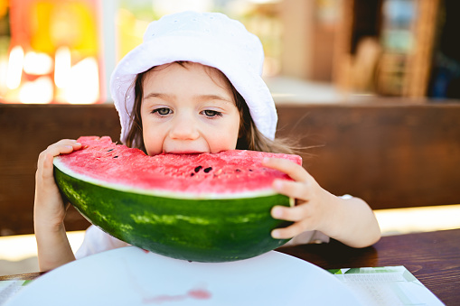 Cute girl eating watermelon on beach bar.