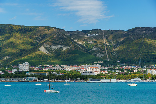 View to small resort town on the Black Sea coast surrounded by greenery. Inscription 'Gelendzhik' on ridge of Caucasus Mountains. Gelendzhik, Russia - September 19, 2022