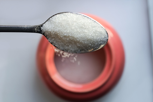 Pour sugar from a teaspoon into a sugar bowl.