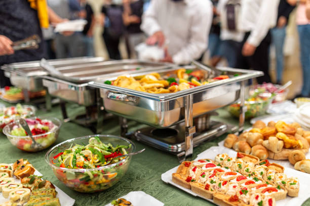 Close up of buffet table food in chafing dish at celebration event. Warming tray with food and people in the background. Party lunch or dinner concept. food service occupation stock pictures, royalty-free photos & images