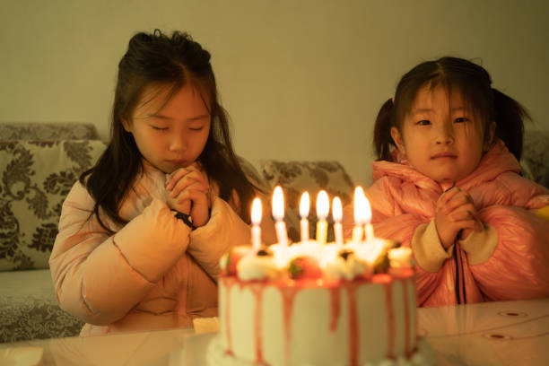 A close-up view of hands holding sticks to light a black birthday cake's candles, surrounded by a festive atmosphere under vibrant, colorful lighting, indicating a party or celebration.