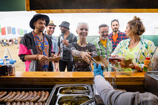 Group of mixed age and ethic friends ordering at a food stall at a festival in Northumberland, North East England. An unrecognisable person is handing a woman her food.
